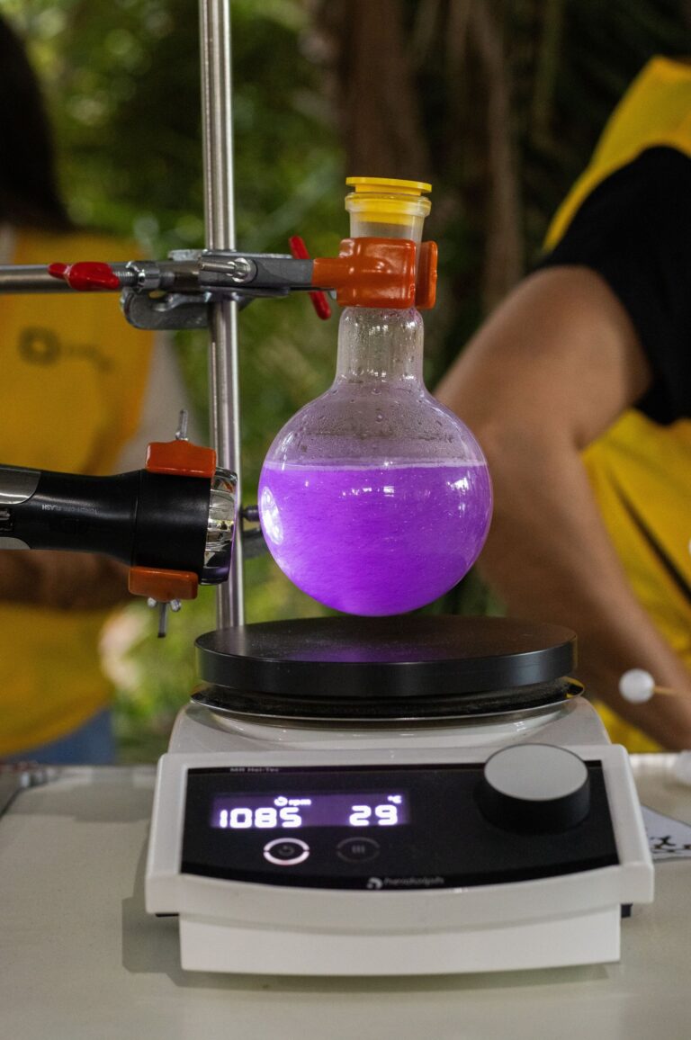 5. Aqui, vemos uma montagem laboratorial com um frasco de vidro contendo um líquido roxo vibrante suspenso sobre uma placa de aquecimento digital exibindo 108°C e 29 rpm, equipado com braçadeiras e uma sonda, ilustrando um processo químico ou reação em andamento nas instalações de pesquisa em química ou nanotecnologia do CNPEM.